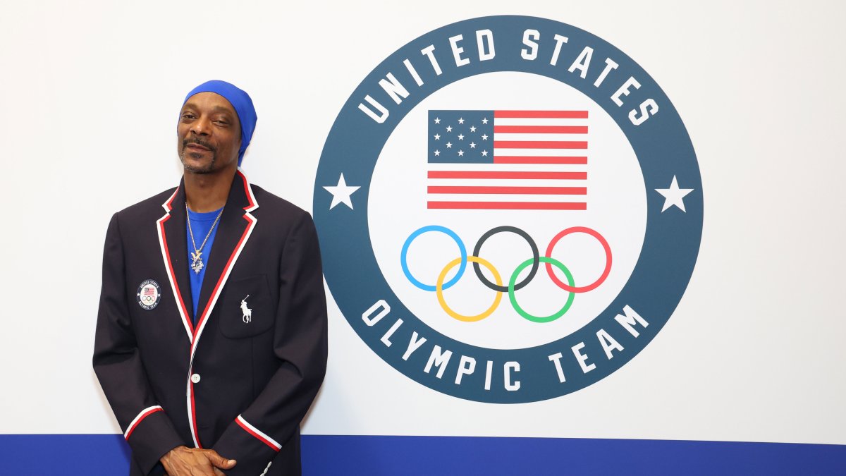 Snoop Doggy Dogg wearing his United States Olympic Team Polo jacket standing by the team emblem. 